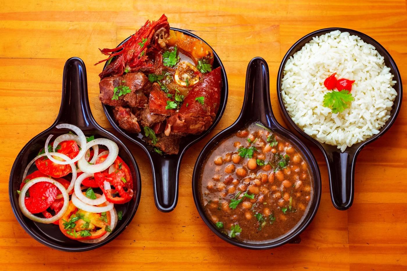 Panelinhas com vinagrete, carne, feijão e arroz sobre mesa de madeira